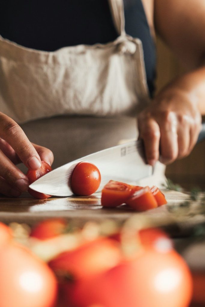 Manos cortando tomates frescos sobre una tabla de madera